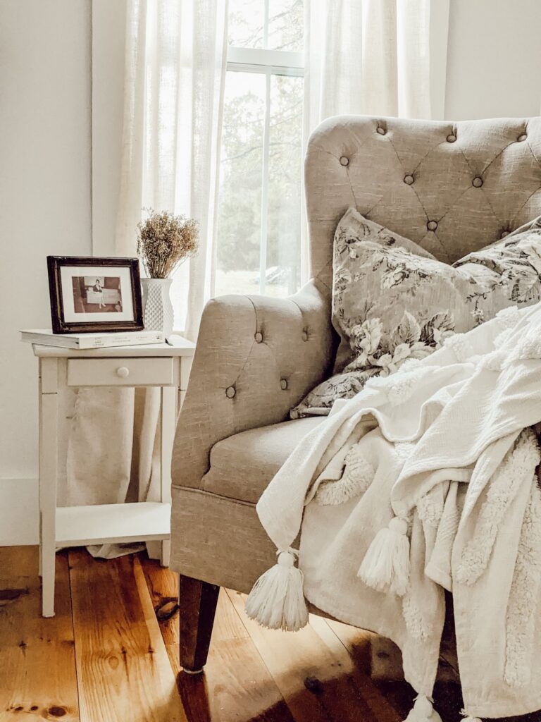farmhouse style sitting area with beige tufted chair with floral pillow and cozy white throw