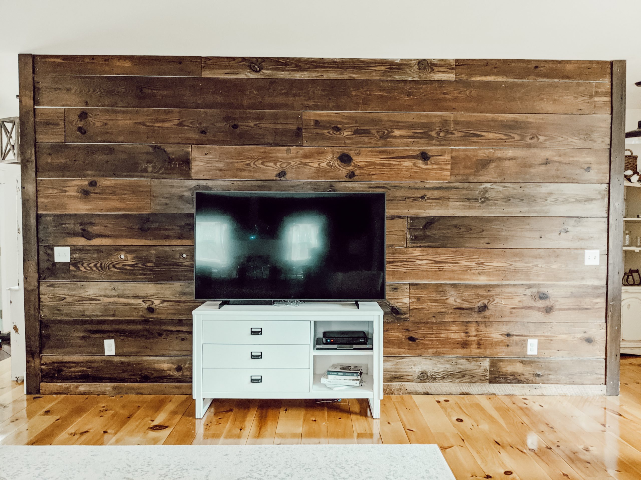 reclaimed wood feature wall in open concept living area, with large tv on white dresser