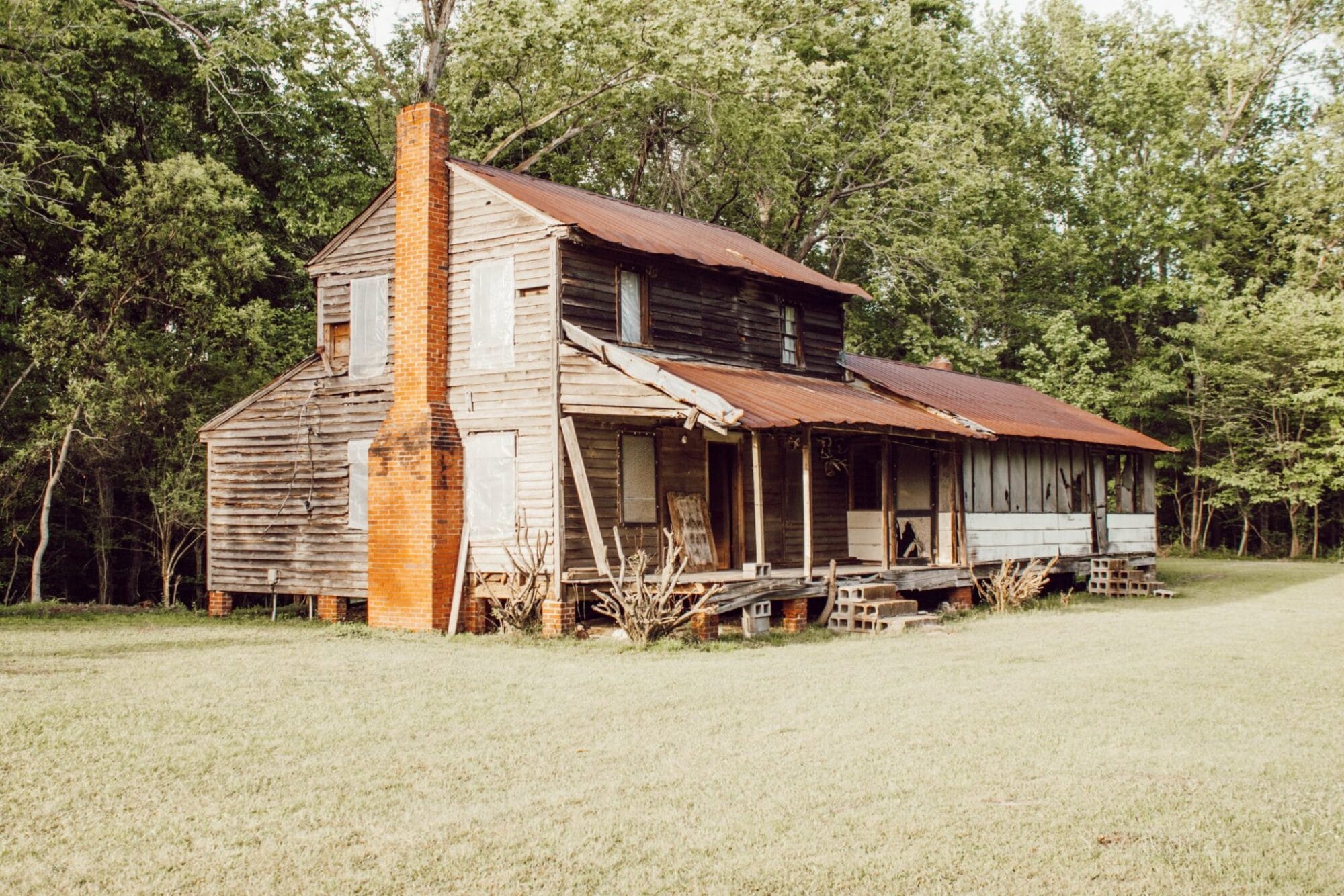 1800's 2 story farmhouse in North Carolina with original wood siding, a brick chimney and a long front porch