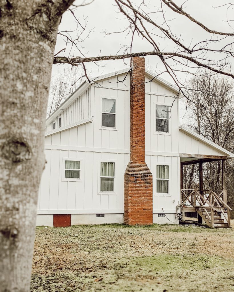 2 story farmhouse with white board and batten siding and red brick chimney