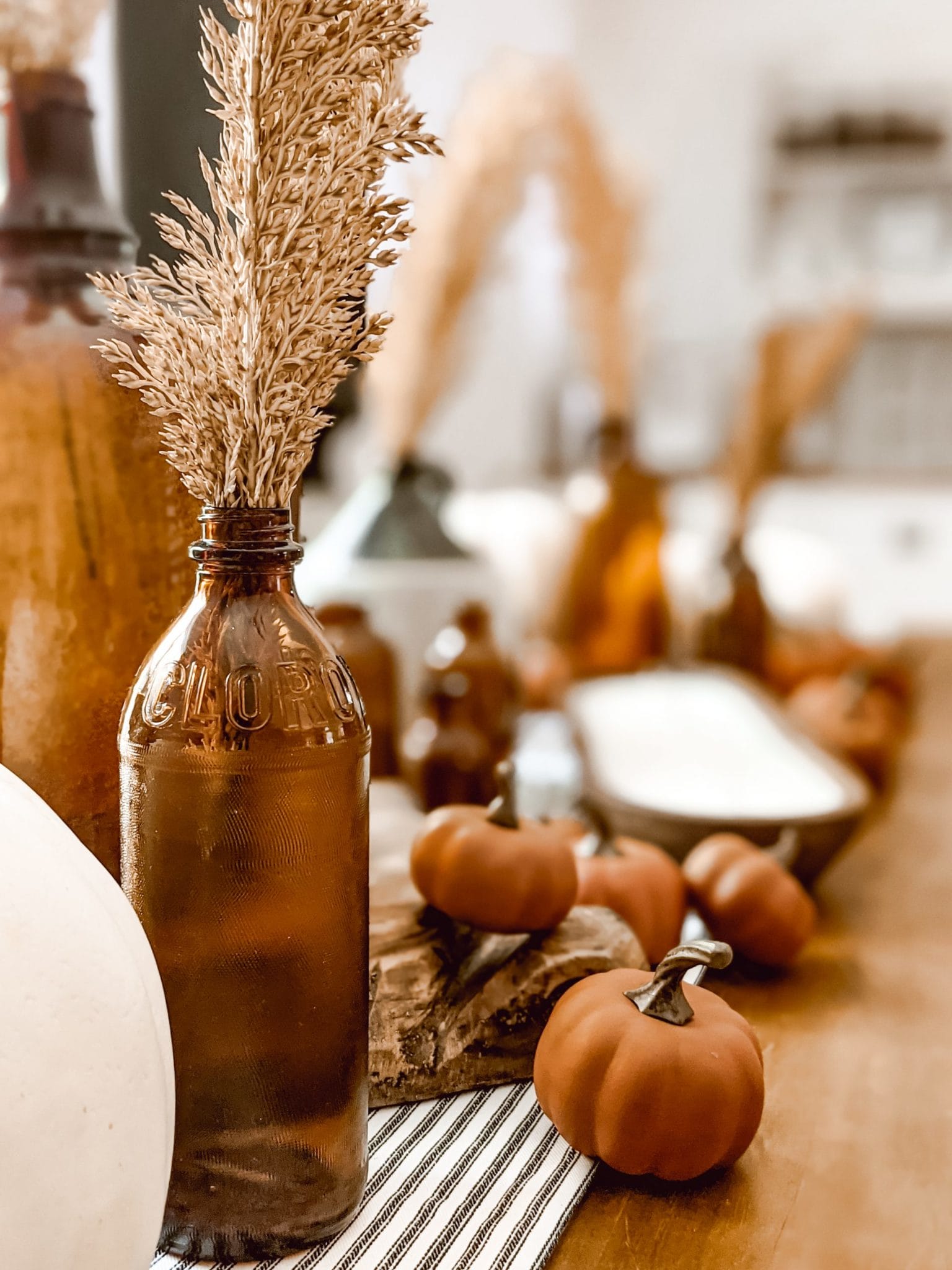 amber glass bottles in a fall dining room centerpiece with white and orange pumpkins