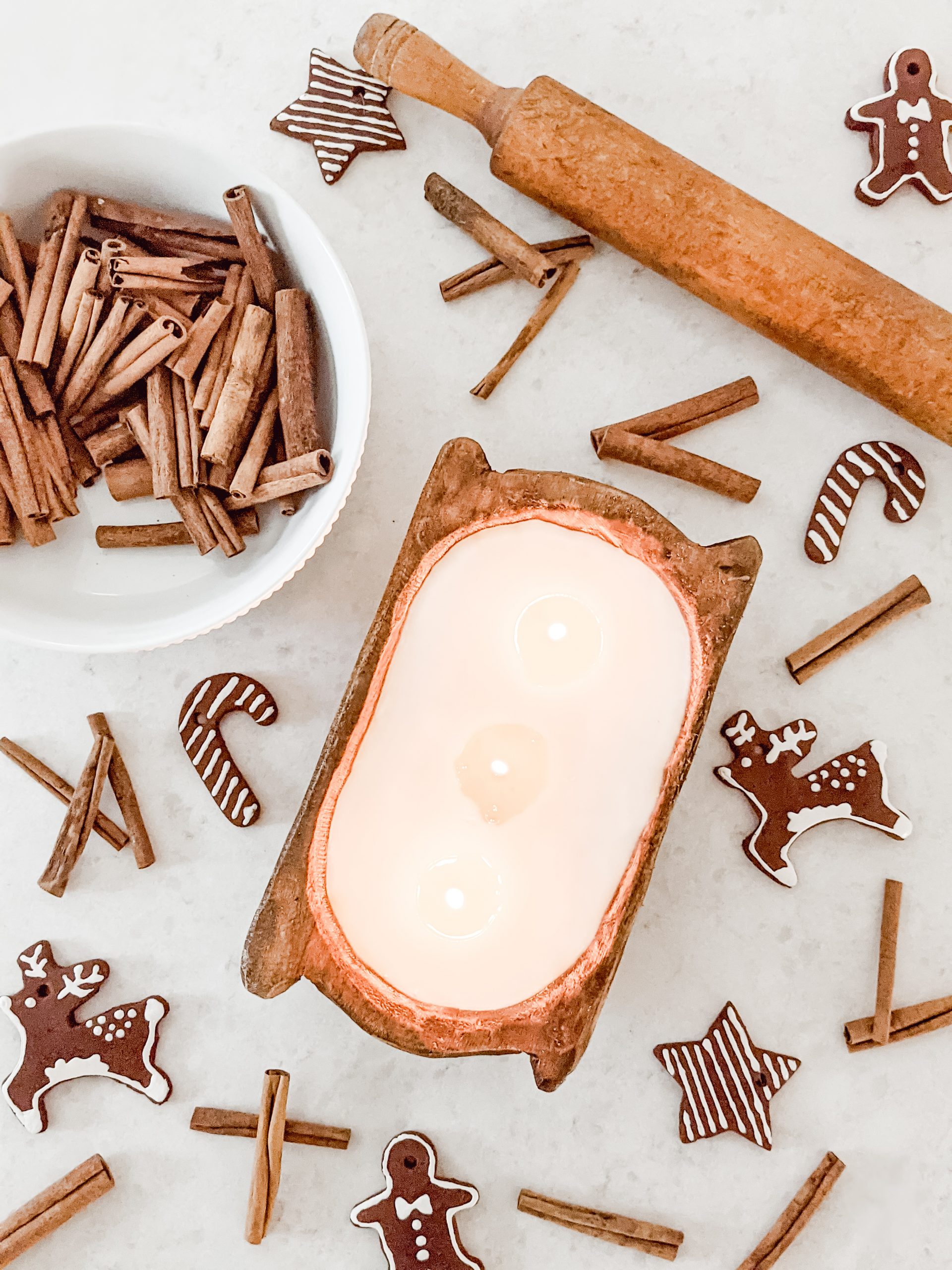 flatlay of doughbowl candle, cinnamon sticks, and DIY iced gingerbread cookie ornaments