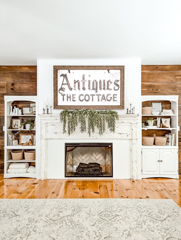 DIY farmhouse fireplace with an antique mantel, built-in shelves, a frame TV above the fireplace, and an electric fireplace insert styled in whites and wood tones
