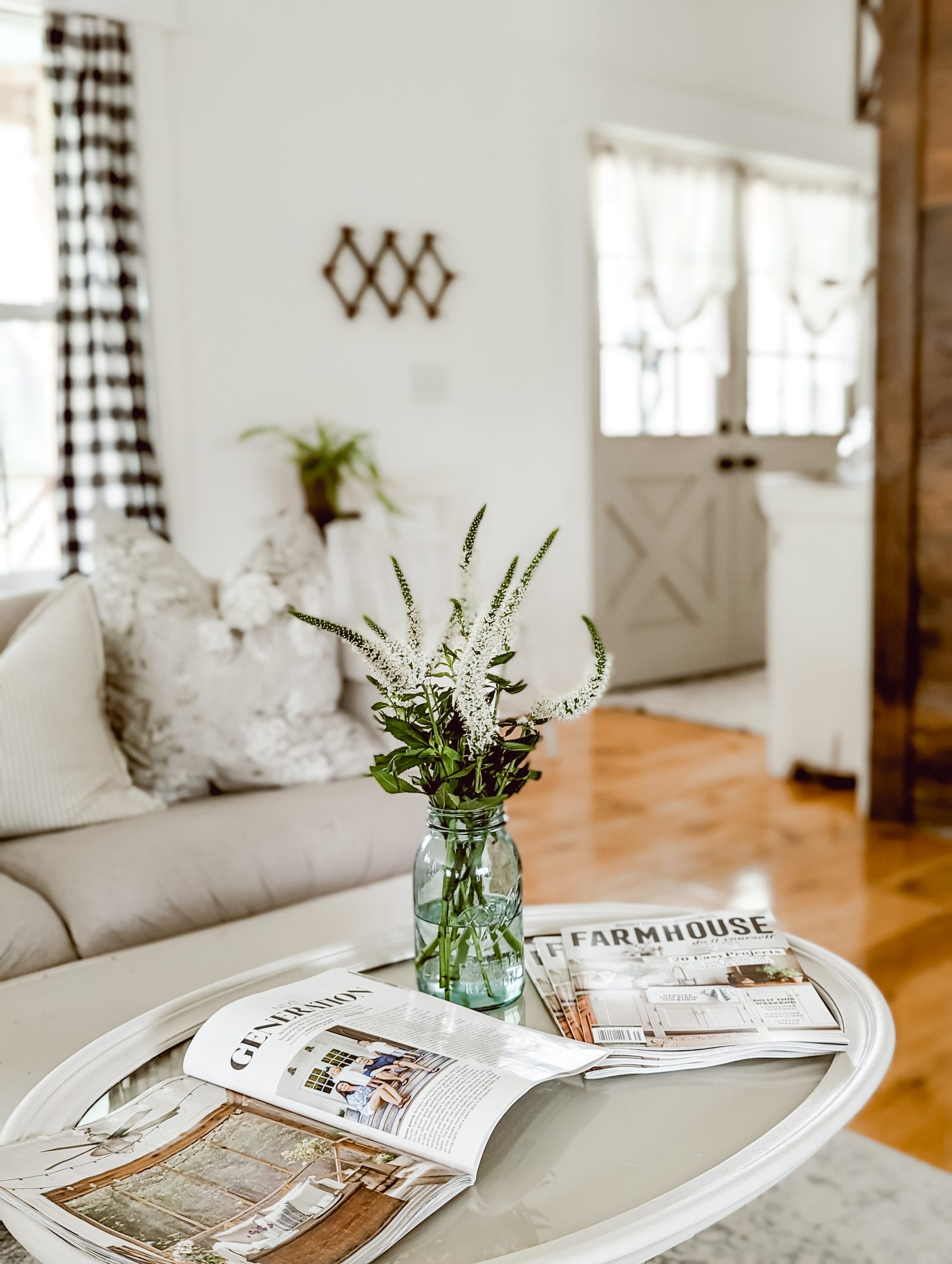 magazines and white flowers in a blue mason jar on a painted oval coffee table