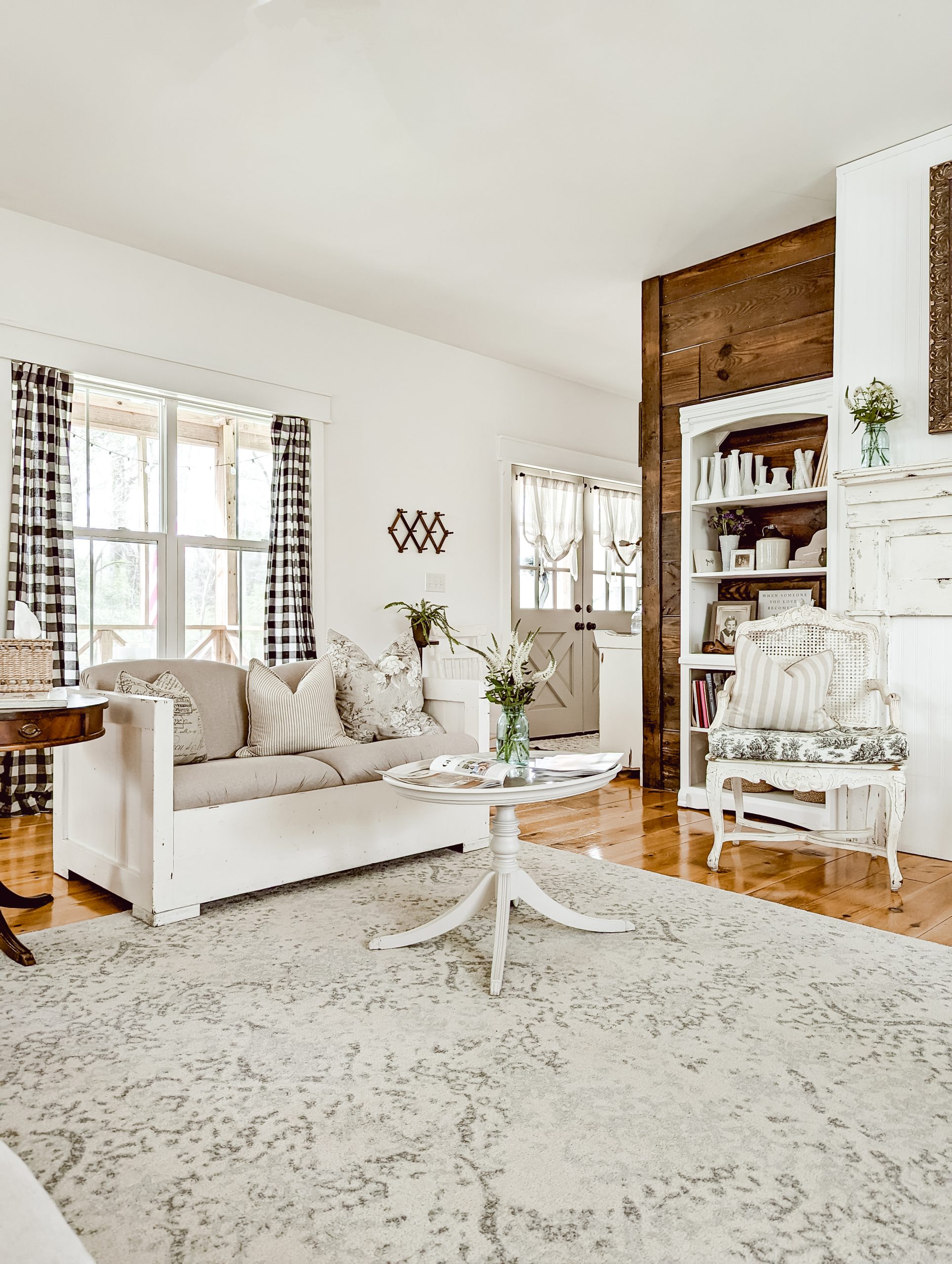 farmhouse living room with white walls, dark stained reclaimed shiplap, white painted furniture, buffalo plaid curtains, pedestal coffee table, cane back sitting chair, 