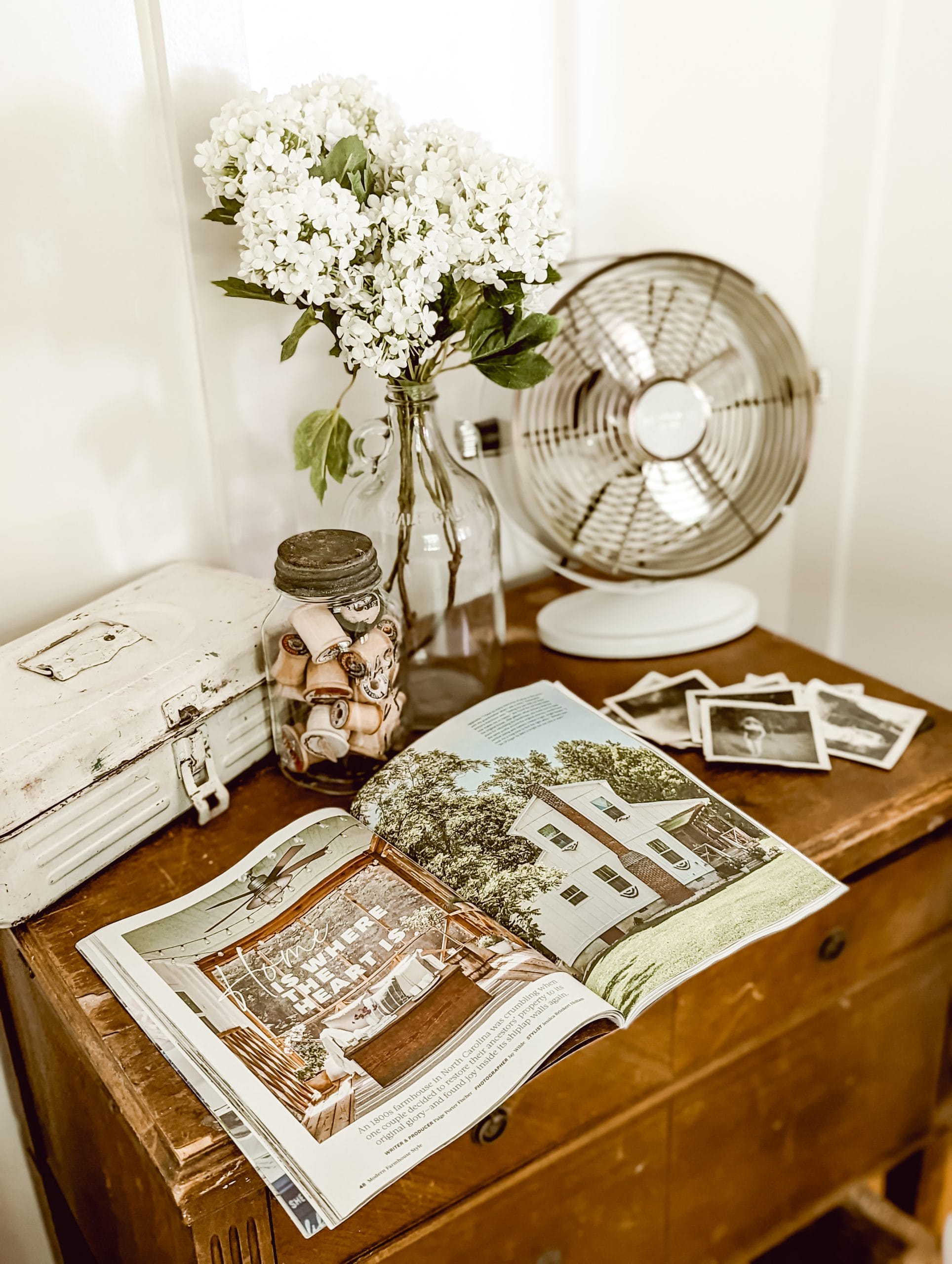 magazine, old black and white photographs, and other vintage decor styled on a wooden side table