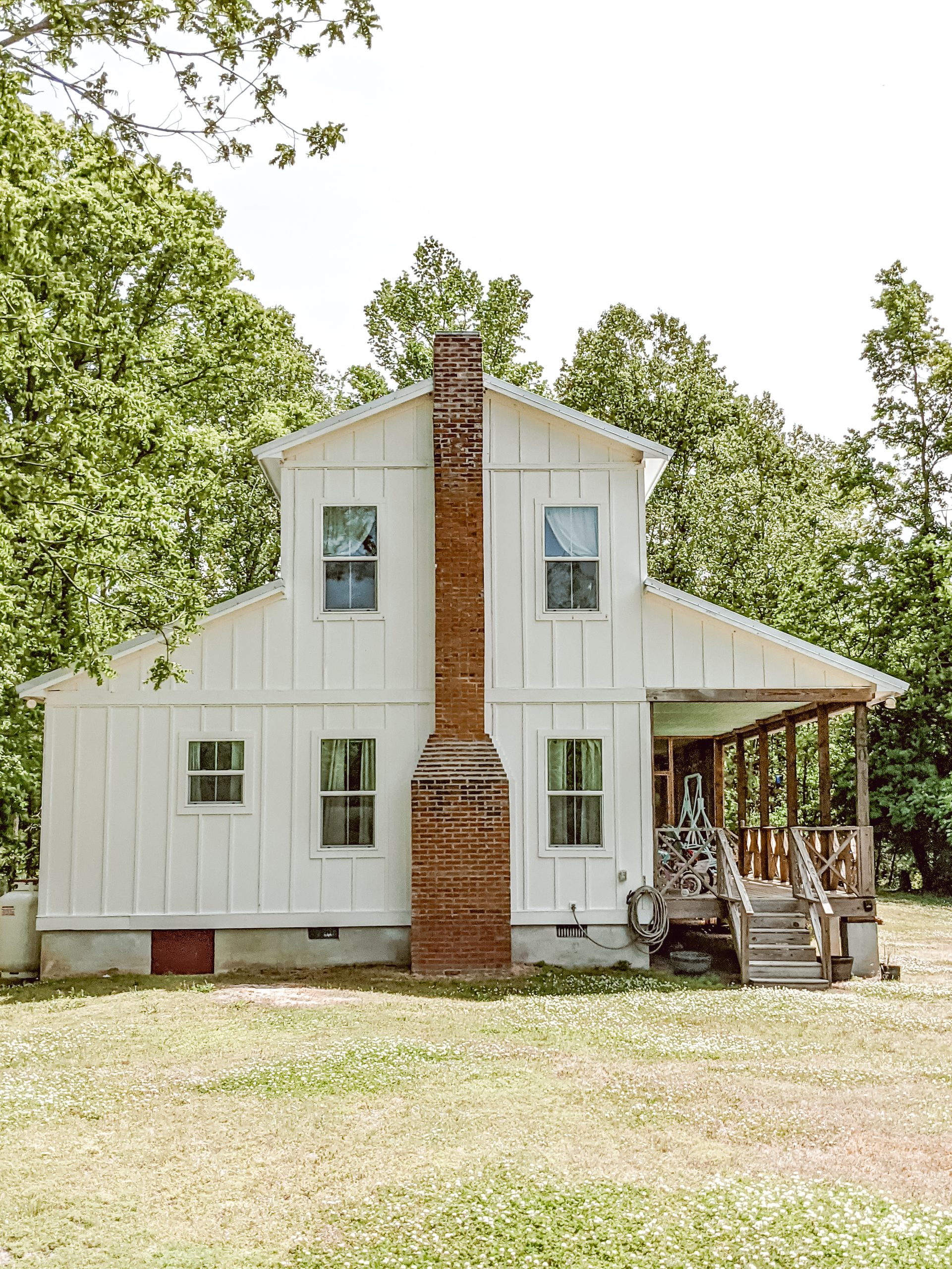 country farmhouse with white board and batten siding and a red brick chimney