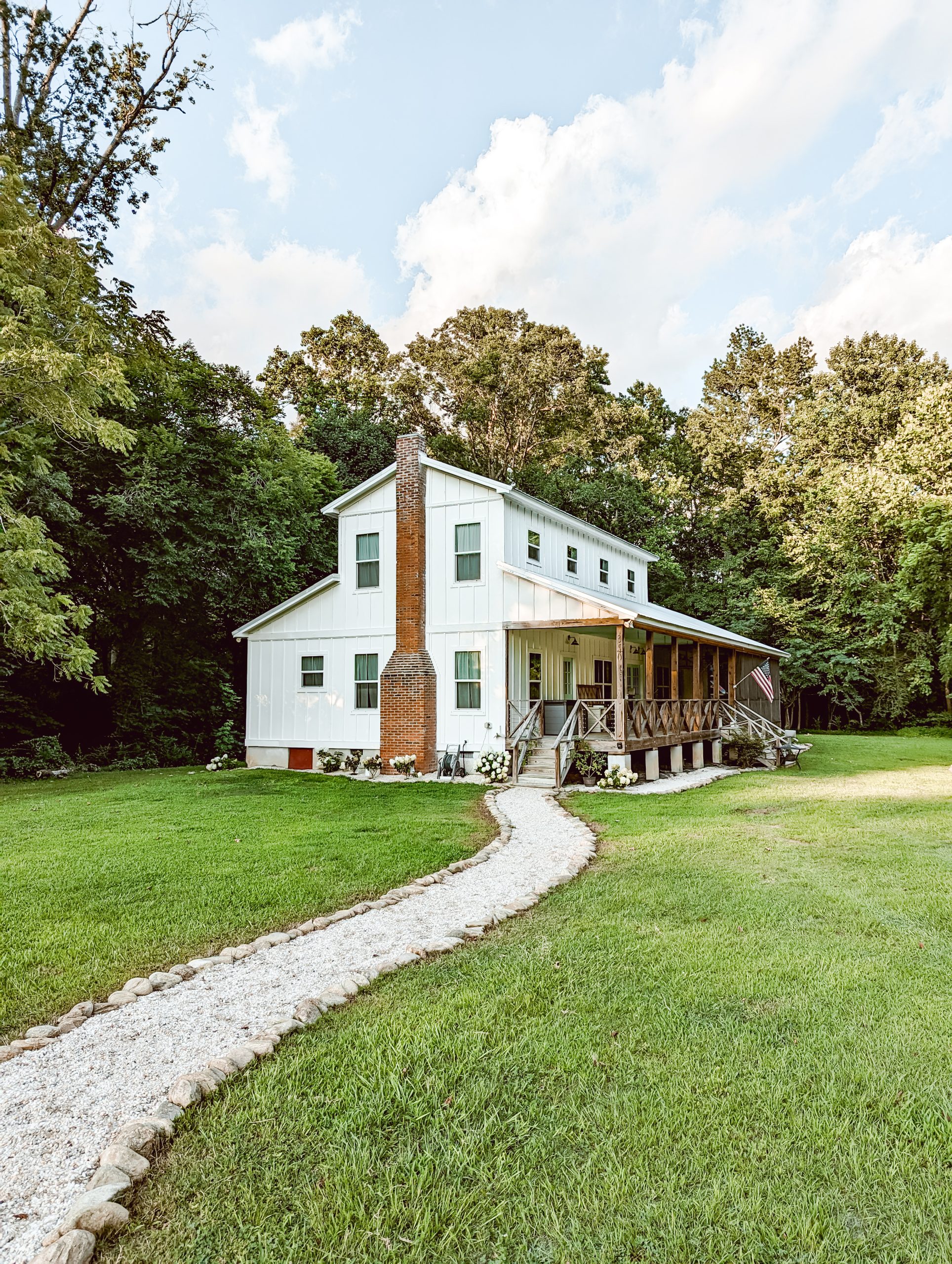 white farmhouse exterior in the country with a pea gravel path leading to the front porch steps