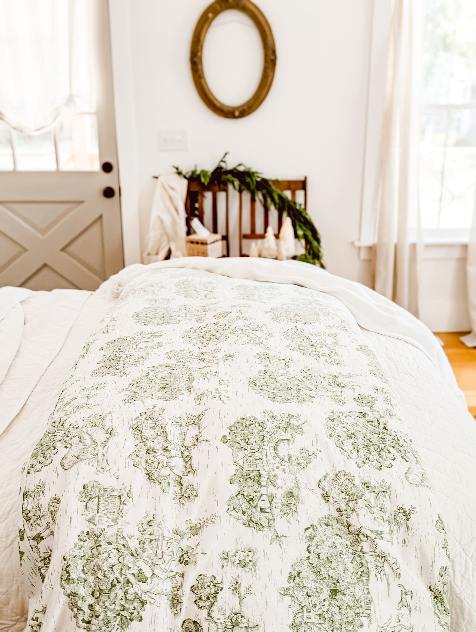 vintage green toile duvet cover draped across the foot of a bed atop a white quilt