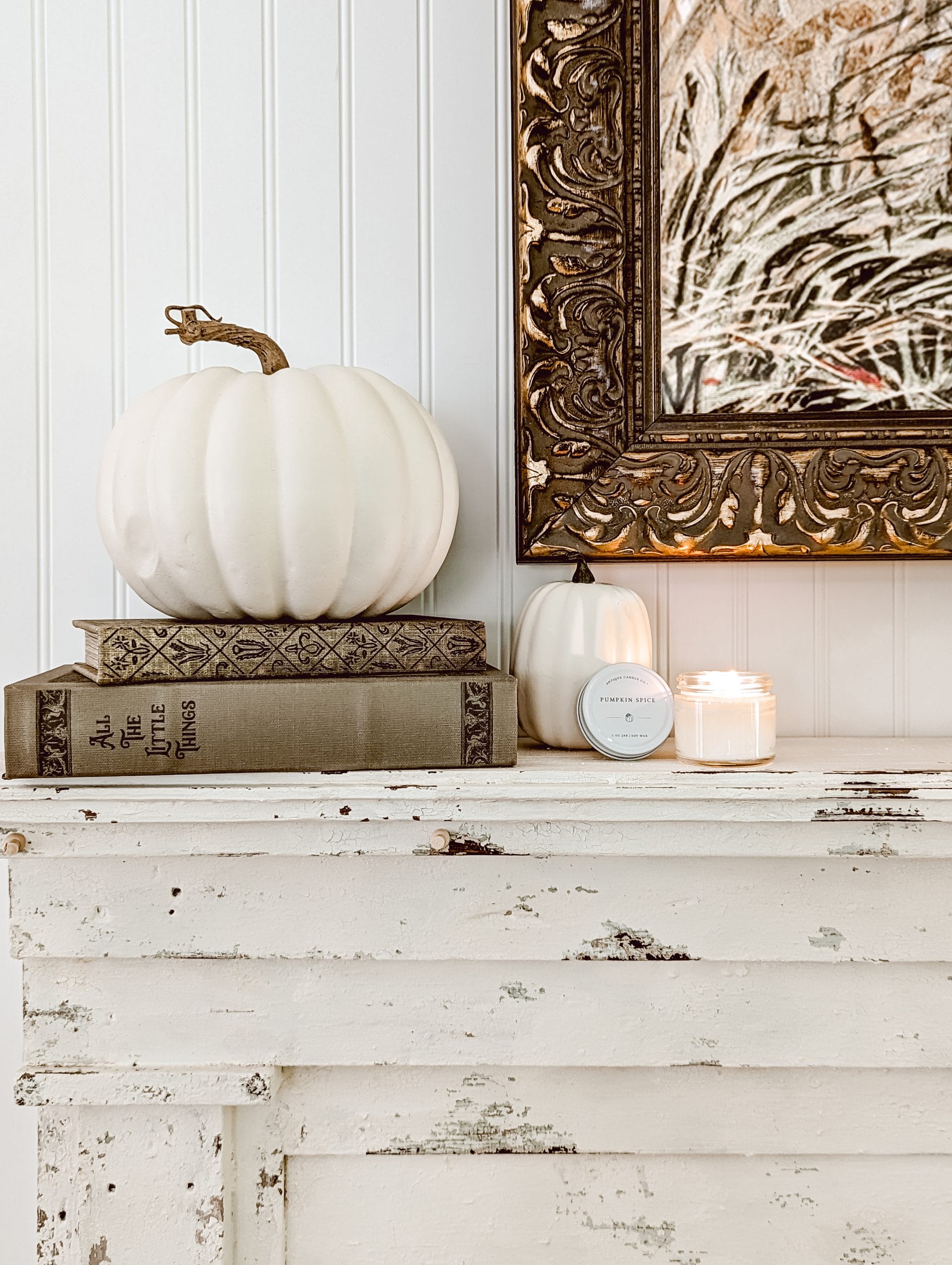 white faux pumpkins and a pumpkin spice candle on a chippy white antique fireplace mantel